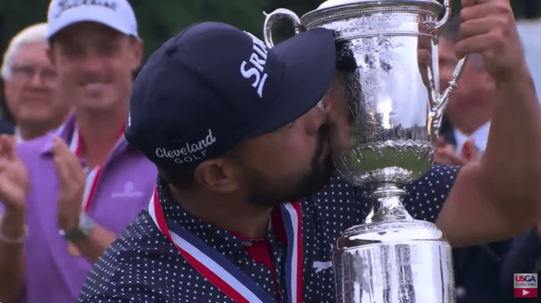 J.J. Spaun kisses the US Open trophy while low amateur Justin Hastings looks on during the trophy ceremony
