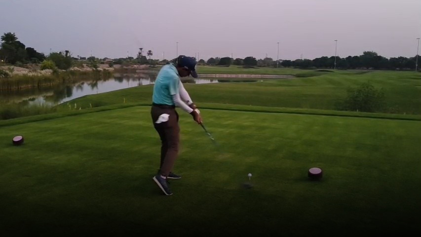 Low angle shot of a golfer's legs and hands holding an iron on a green, with no ball present